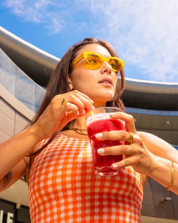 Shooting Waffle Factory : femme en lunettes jaunes tenant une boisson fruitée sous un ciel bleu, direction artistique solaire